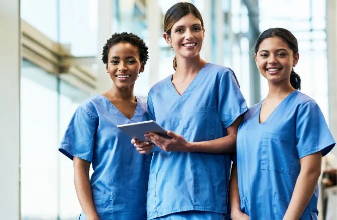 A smiling group of women dentists wearing blue scrubs